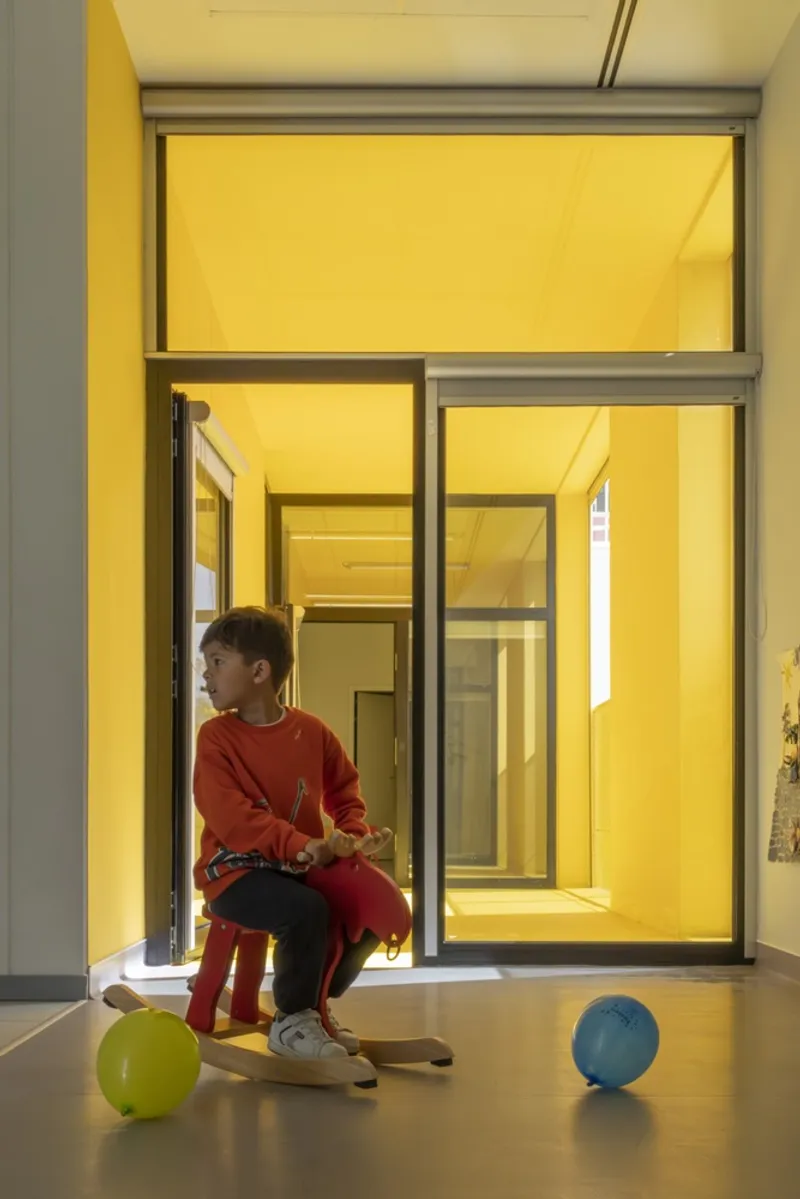 Child on a red toy horse in a threshold between grey flooring and yellow interior rooms