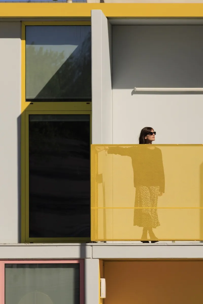 Yellow balcony railing with a person standing behind the translucent parapet in bright sunlight