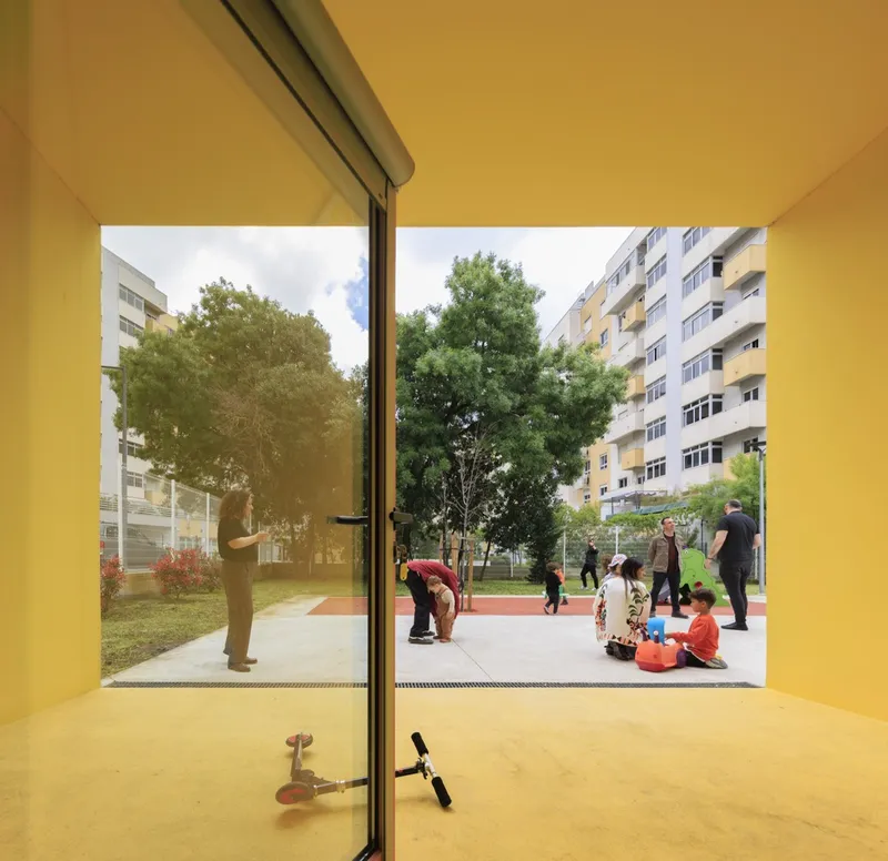 Yellow interior looking out to courtyard with families, trees, and residential buildings in sunlight