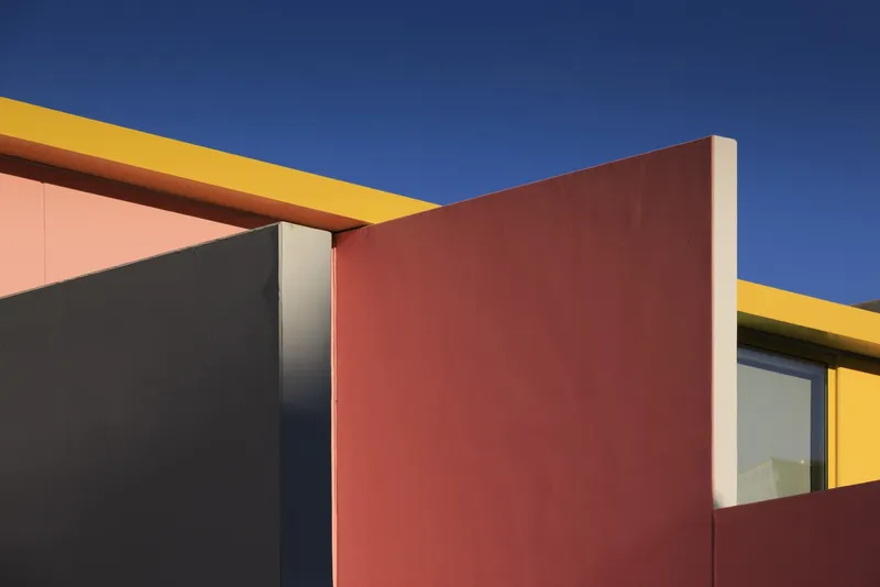 Intersection of yellow beam, terracotta wall and gray panel under clear blue sky