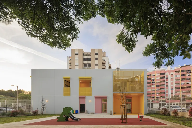 Garden elevation with white panels, yellow openings and playground equipment framed by overhanging tree branches