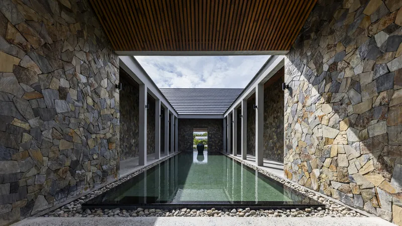 Reflecting pool flanked by mosaic stone walls under a timber slat ceiling