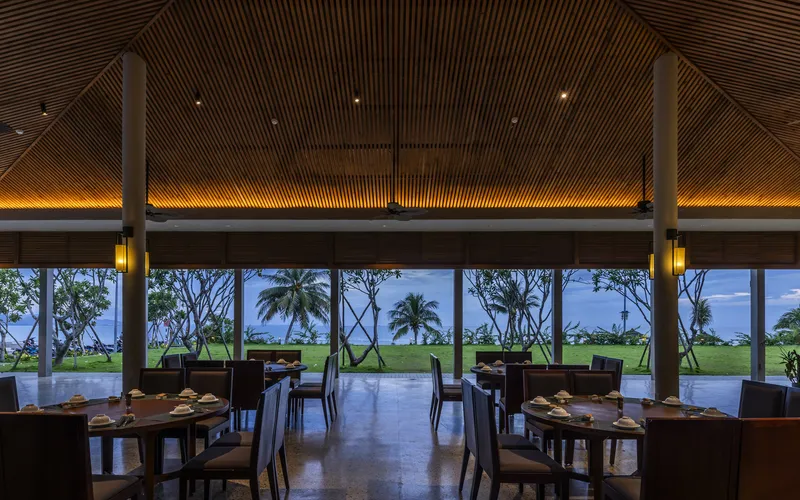 Restaurant interior framing palm trees and lawn through floor-to-ceiling glazing at twilight