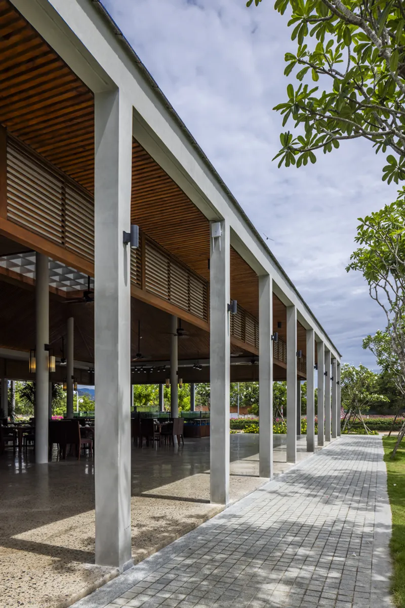 Covered colonnade with white concrete columns and timber slat soffit beside planted lawn