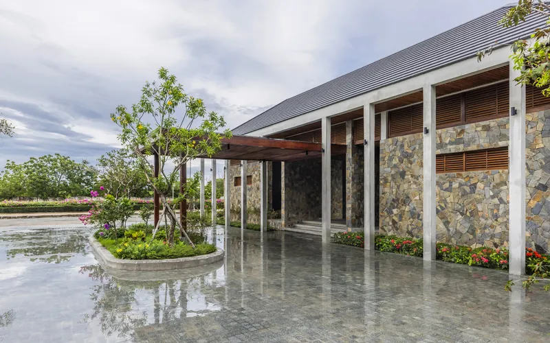 Covered colonnade with white columns and mosaic stone walls alongside a wet paved courtyard after rain