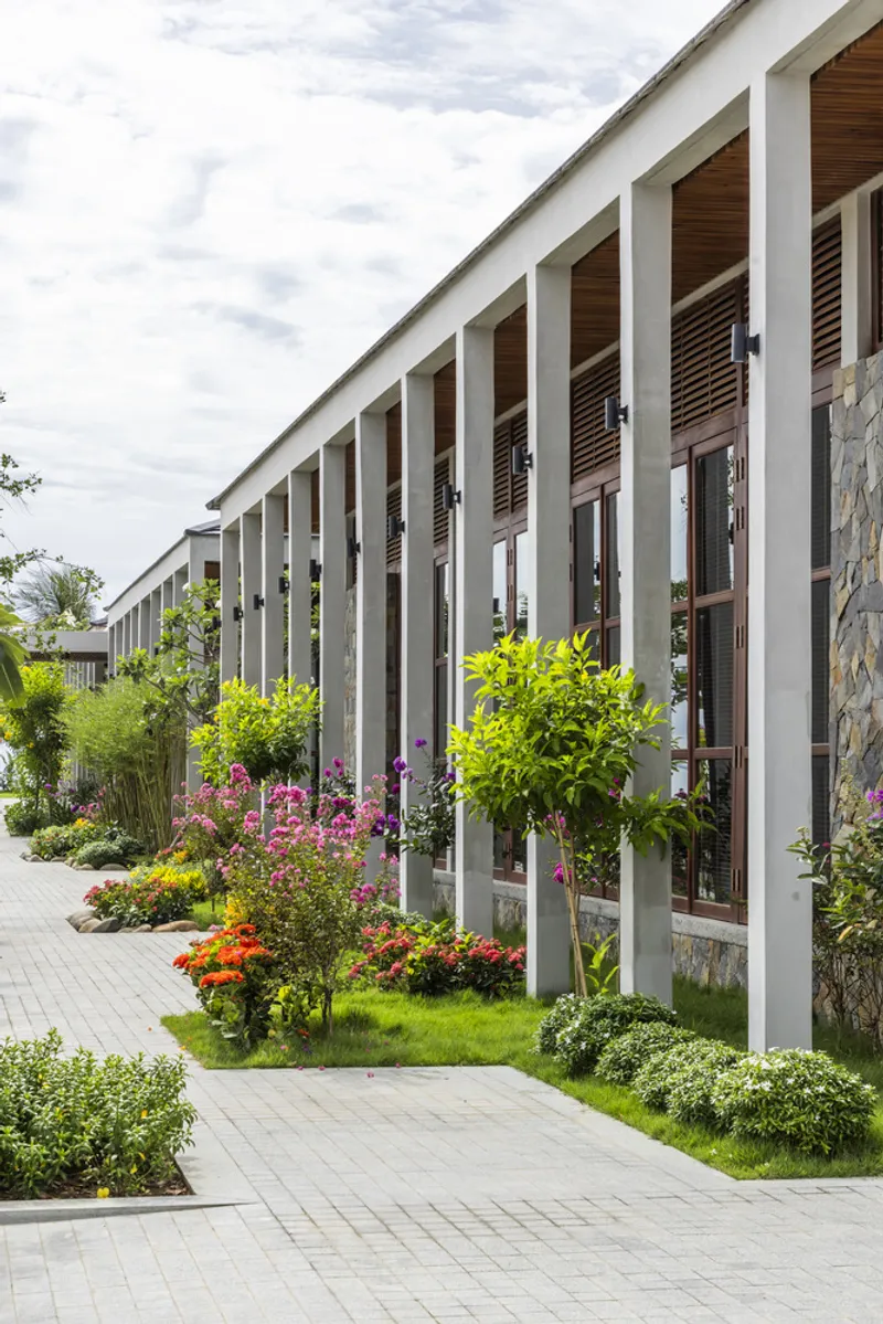 Street view of the colonnaded facade with timber louvers and planted beds of flowering shrubs