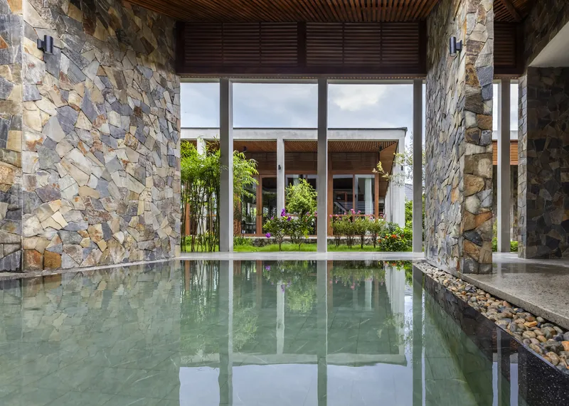 Interior reflecting pool flanked by curved stone walls beneath a timber slatted ceiling