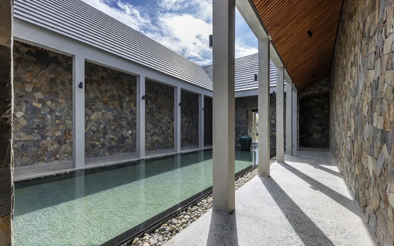 Covered walkway beside a shallow pool with pebble edging under afternoon shadows