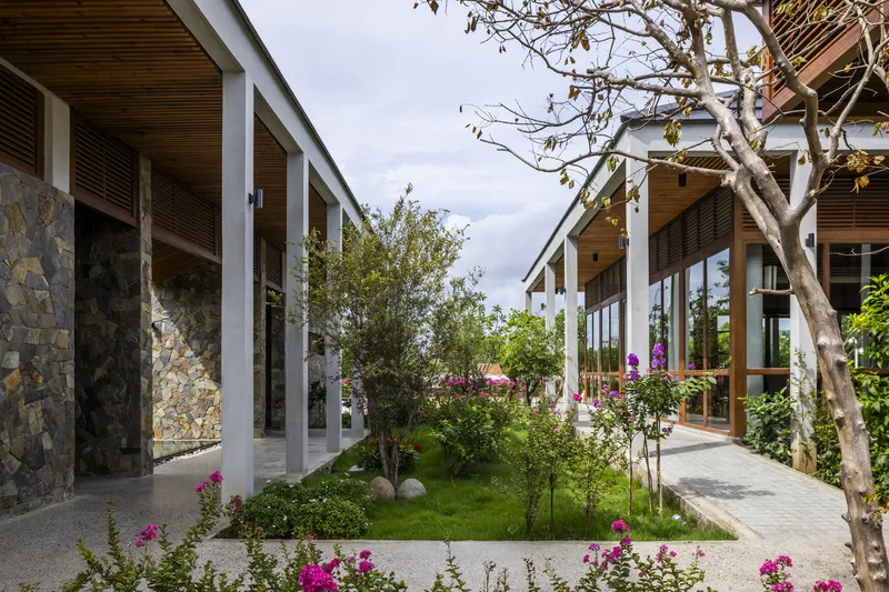 Covered walkway with stone columns and timber soffit overlooking a planted courtyard with flowering shrubs and bare trees