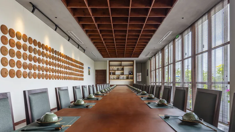 Long dining table beneath a timber coffered ceiling with circular wall installation and slatted blinds filtering daylight
