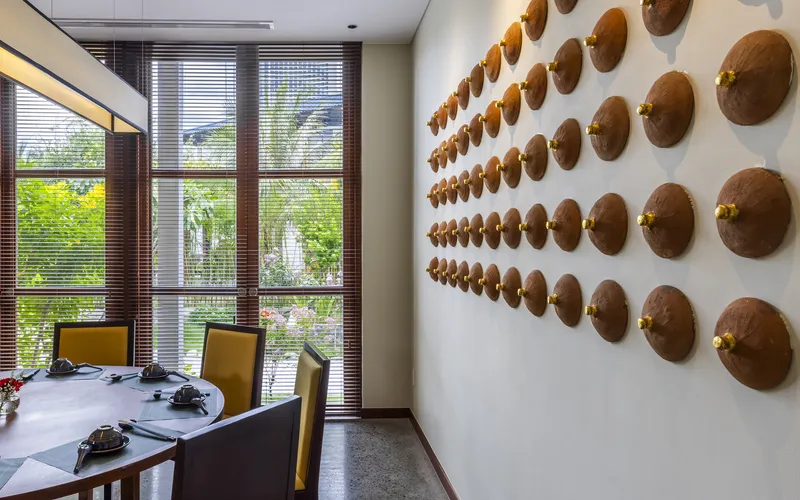 Dining area with circular copper discs mounted on white wall and wooden blinds overlooking green courtyard