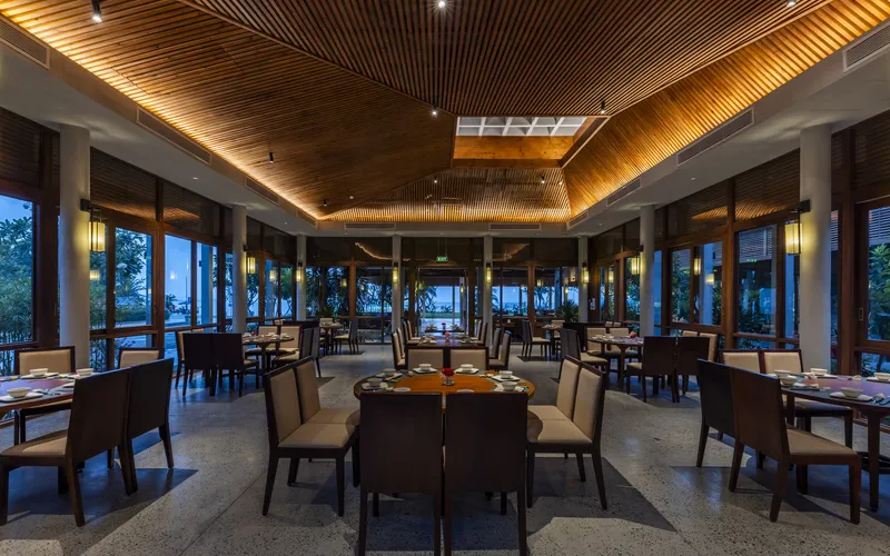 Dining room with illuminated timber slatted ceiling and floor-to-ceiling windows facing the water at dusk