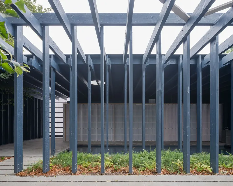 Covered exterior walkway with vertical steel columns and overhead beams framing a planted courtyard bed