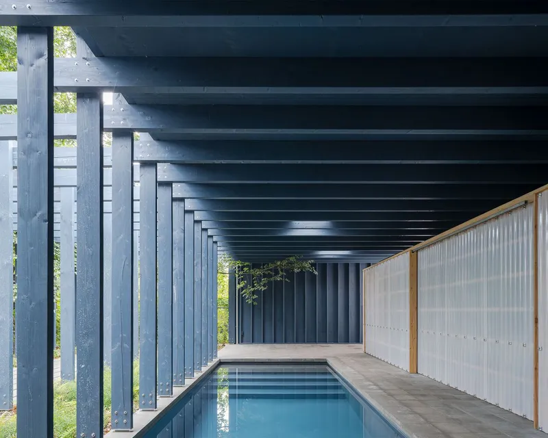 Covered pool area with exposed steel beam ceiling and translucent corrugated panels along one side