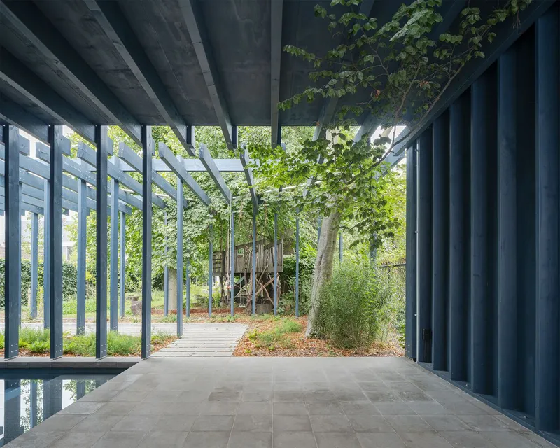 View through the steel pergola structure toward surrounding trees and a timber walkway in dappled sunlight