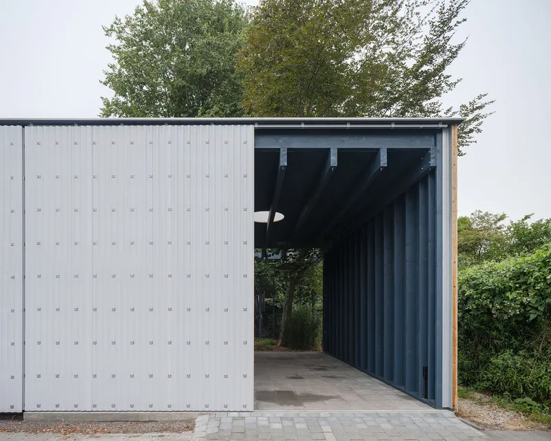 Exterior facade with sliding white corrugated panel and vertical steel columns framing the entrance threshold