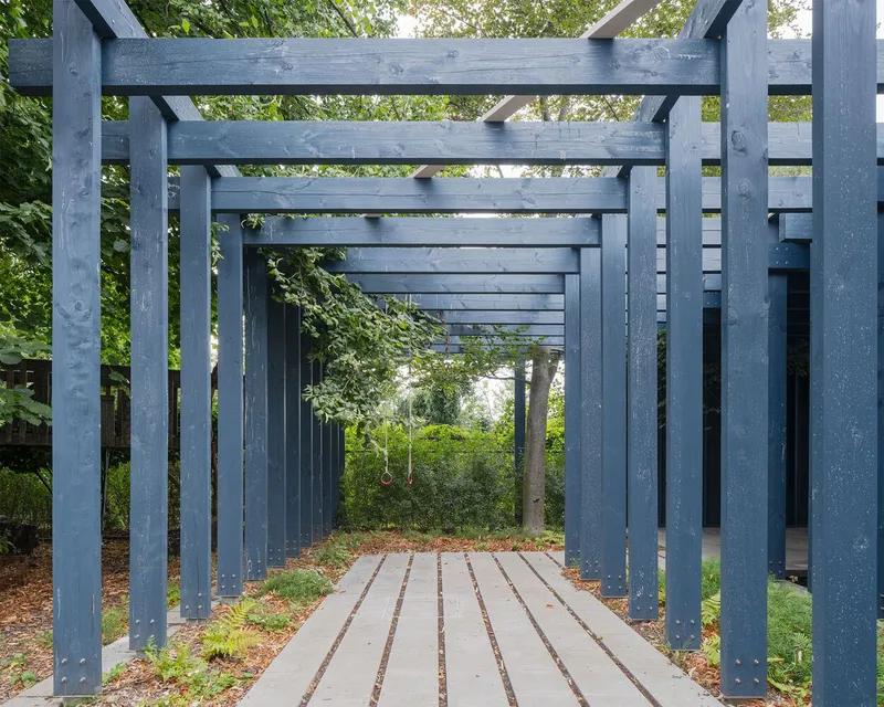 Covered timber walkway with blue-grey columns and exposed beams framing a view through dense foliage