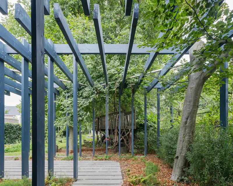 Pergola with angled timber rafters and vertical posts surrounding mature trees in a planted garden