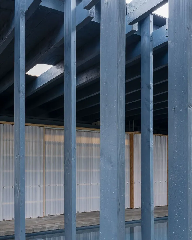 Close-up of timber columns and beams framing translucent corrugated panels at dusk