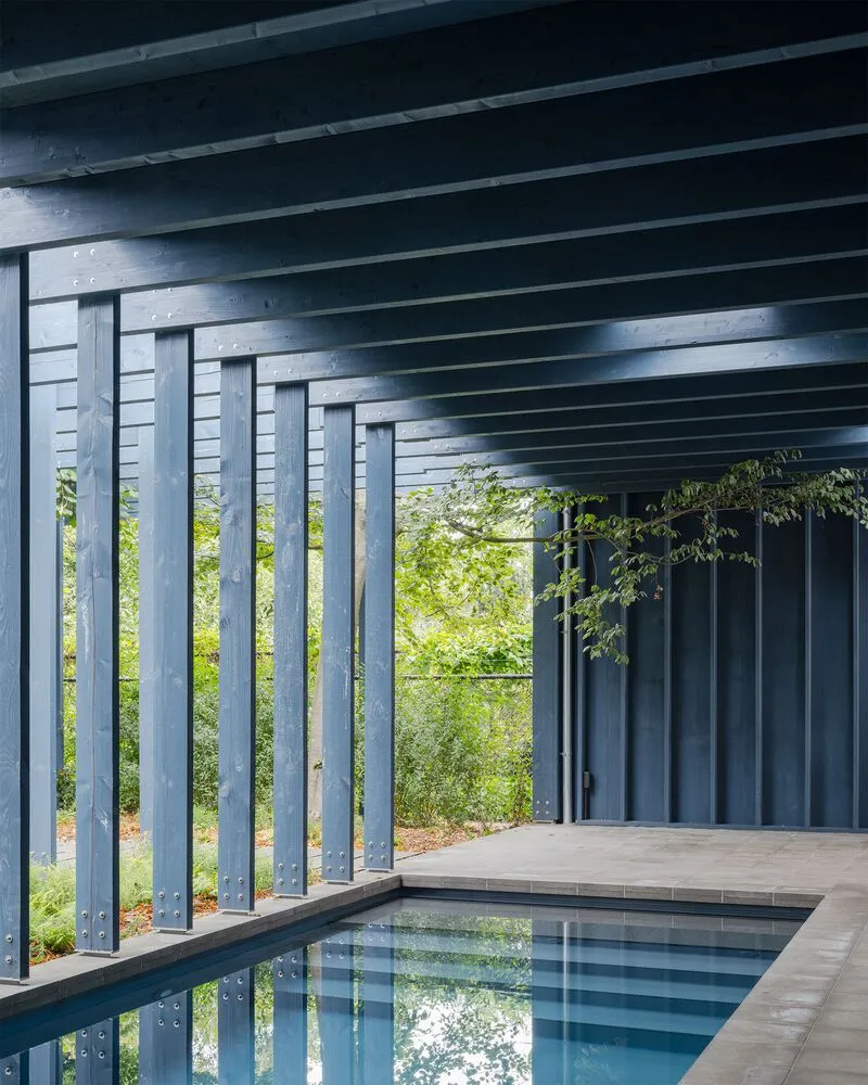 Covered pool terrace with timber columns and black soffit overlooking green landscape through vertical batten screen
