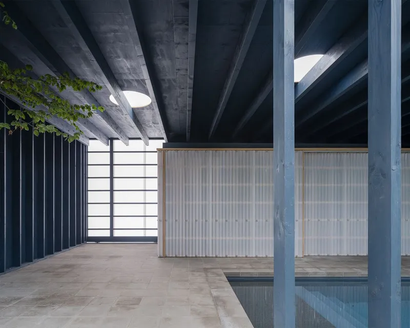 Interior pavilion space with exposed timber structure, corrugated wall panels and reflecting pool below
