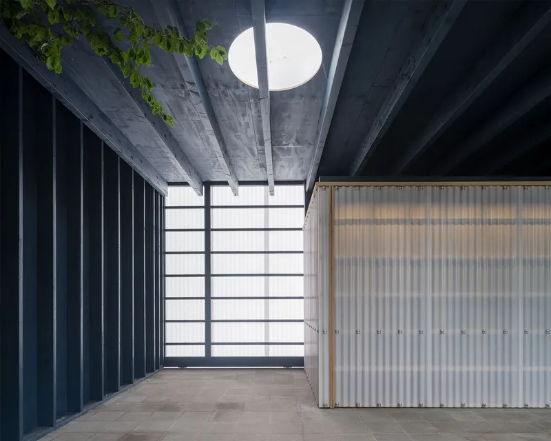 Interior courtyard with circular skylight above exposed concrete beams and corrugated metal wall