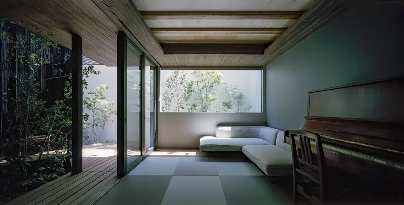 Tatami mat room with timber ceiling beams and sliding glass doors framing a planted courtyard with bamboo
