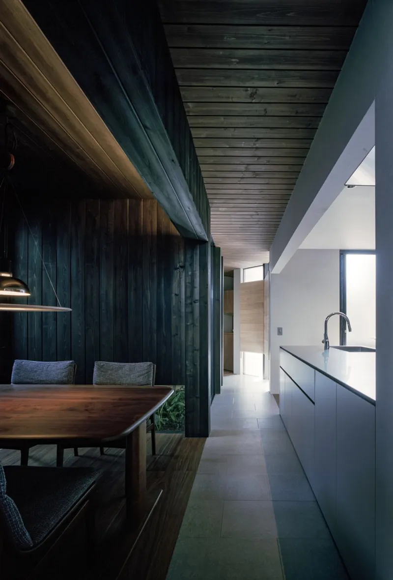 Corridor with dark timber wall panels and timber plank ceiling alongside a white galley kitchen in afternoon light