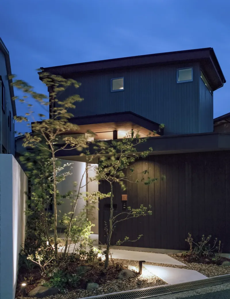 Street view of the corrugated metal facade and entry pathway with young trees and gravel at dusk