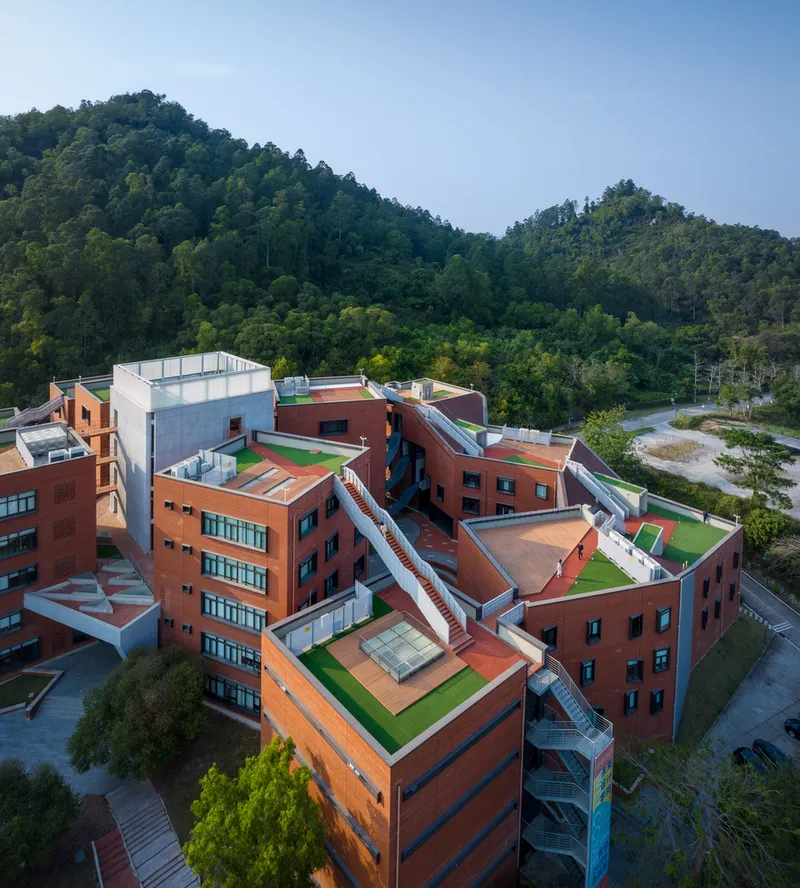 Aerial view of clustered brick volumes with green rooftop terraces nestled against forested hills