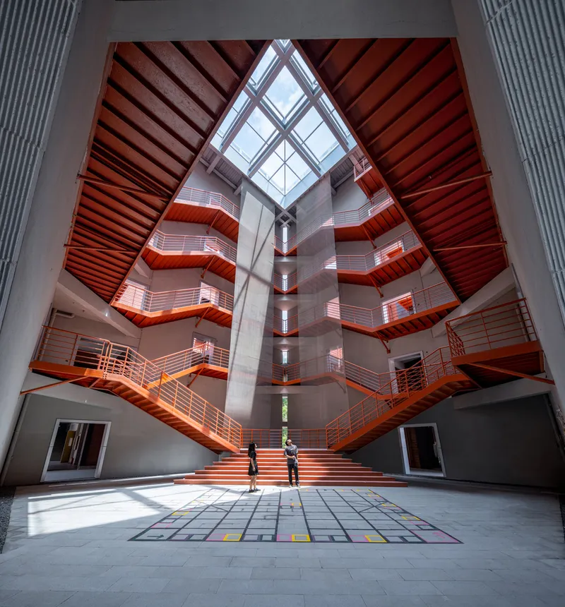 Interior atrium with zigzagging orange staircases and balconies rising beneath a pyramidal skylight