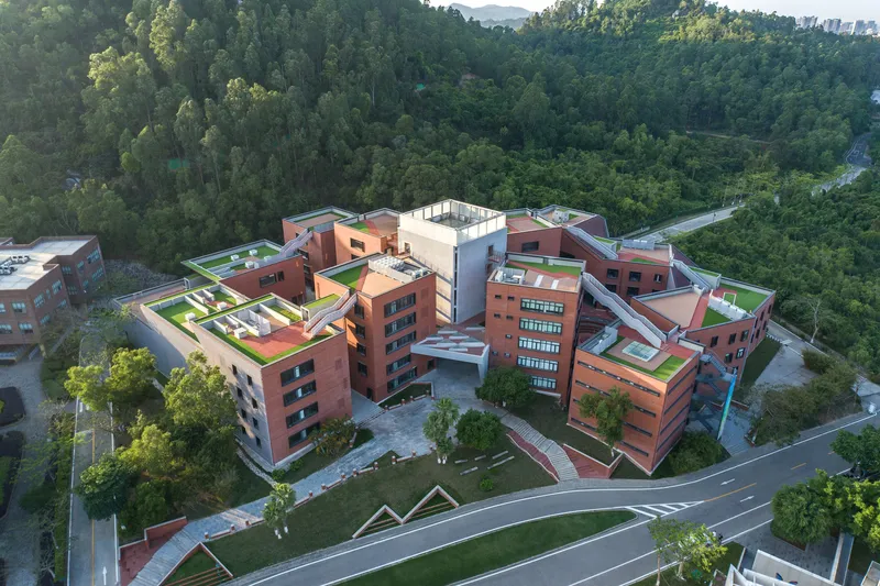 Drone view of the campus complex with green roofs and a zigzag road approaching through trees