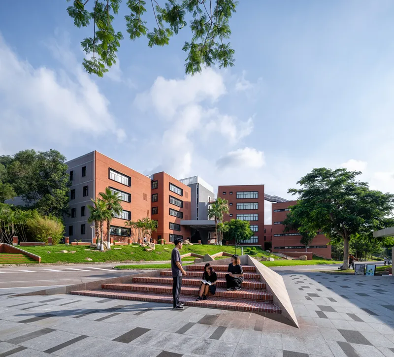 Exterior plaza with angular brick bench and paving where students gather beneath tree canopy