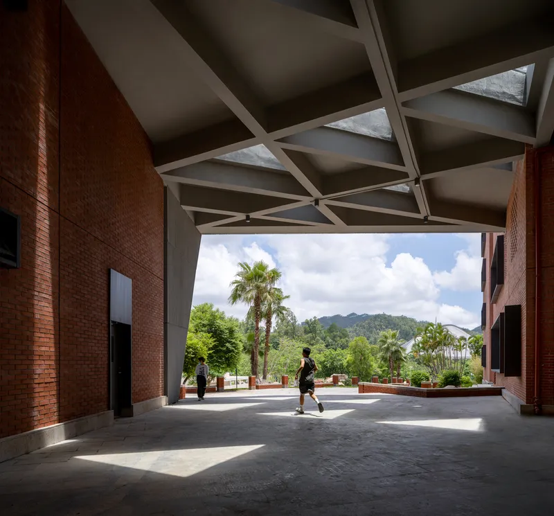 Covered passage with angular concrete ceiling beams framing a view of palm trees and hills