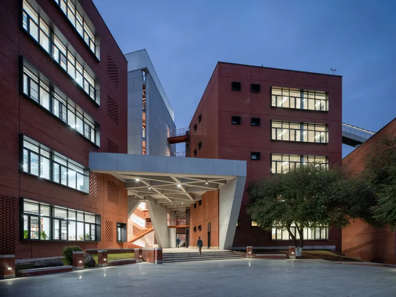Angular white canopy entrance connecting red-paneled volumes at dusk with interior lighting visible