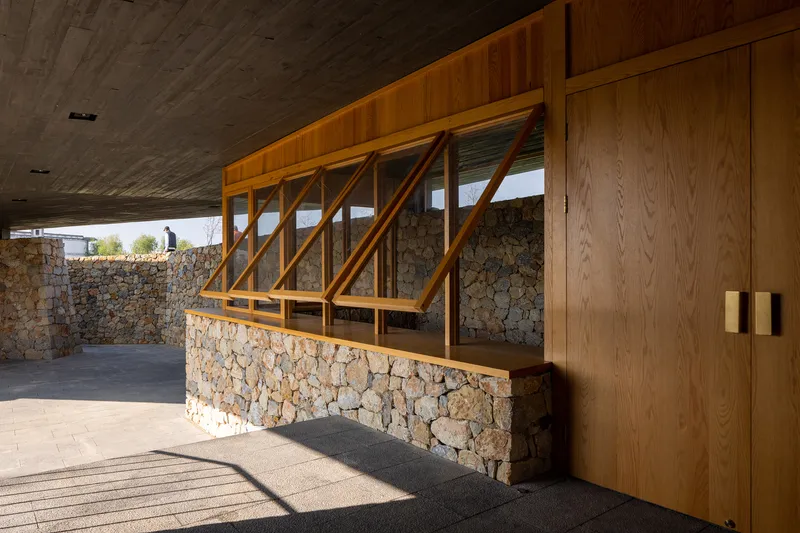Covered terrace with angled timber window frame above a stone wall base and concrete ceiling