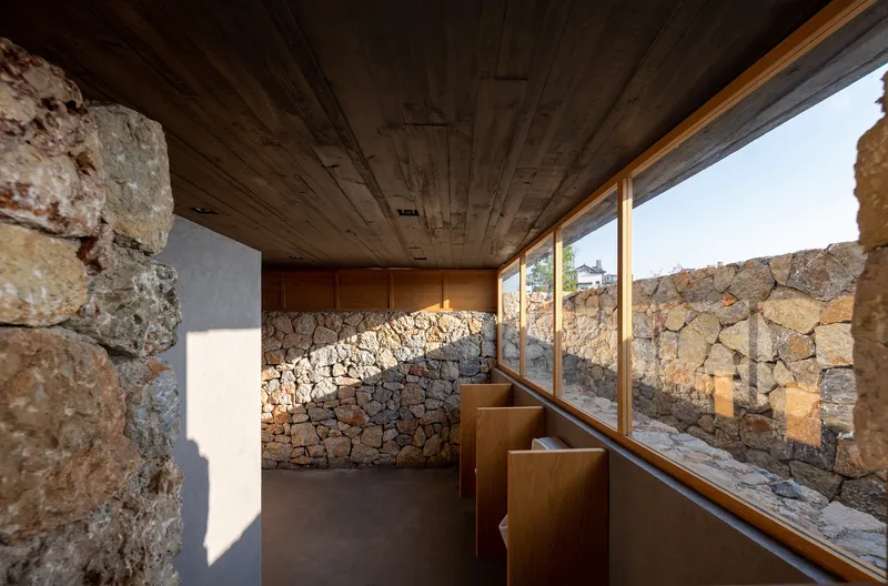 Interior corridor with timber ceiling and window wall overlooking stone courtyard in afternoon light