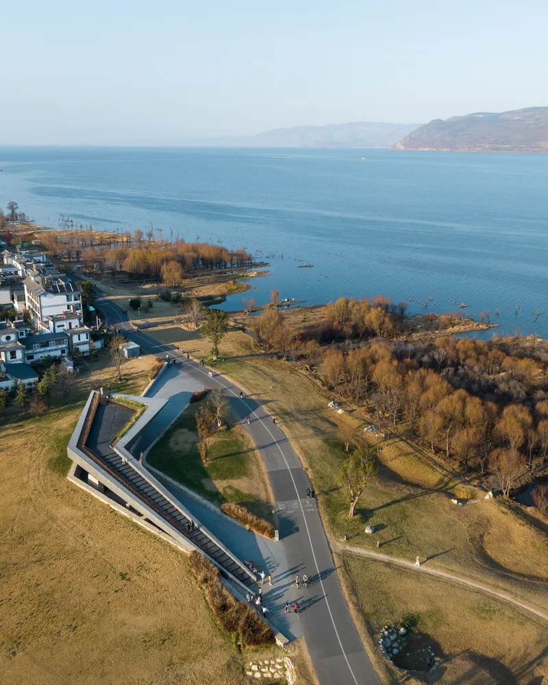 Drone view of the angular roof structure beside a lake with bare trees and distant mountains