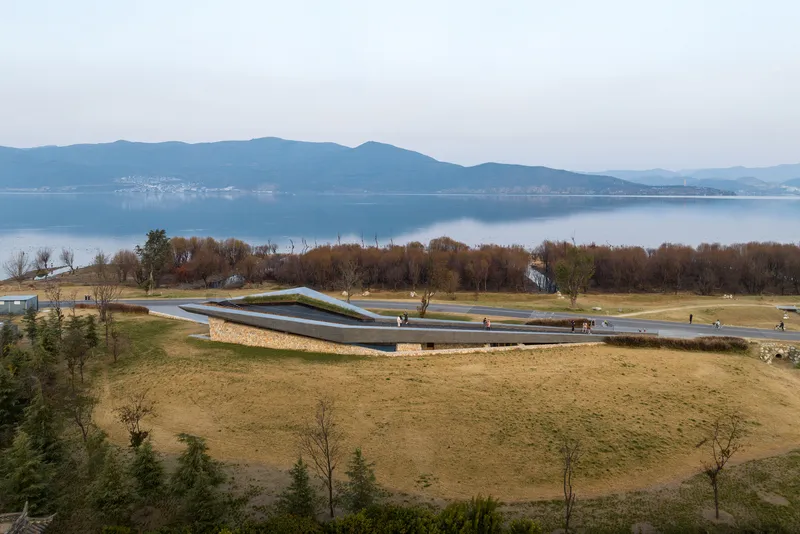 Long view of the folded roof form in a lakeside park with visitors and scattered trees