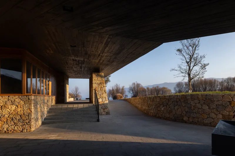 Exterior walkway under a deep roof overhang with stone walls and bare winter trees beyond