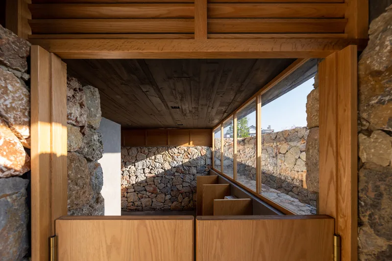 View through timber doorway showing a stepped stone courtyard and glazed opening to landscape beyond