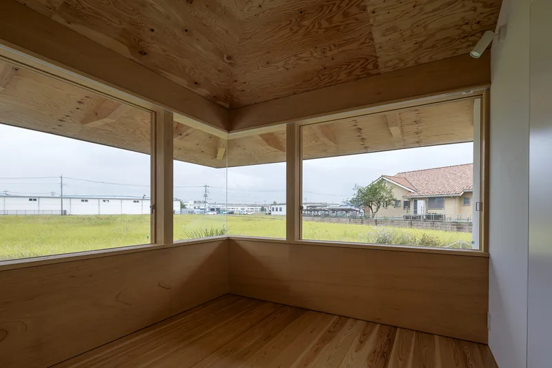 Corner window alcove with plywood ceiling and timber sill overlooking open fields