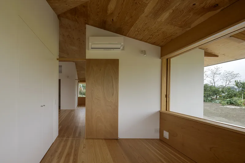 Interior room with plywood ceiling and walls, timber flooring, and a large corner window overlooking vegetation