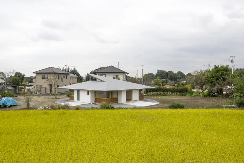 White pavilion with overhanging pyramidal roof and curved terrace set within a golden rice field