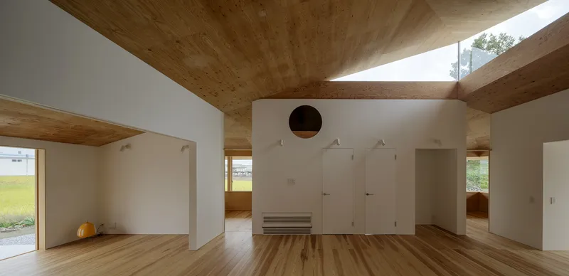 Open-plan interior with plywood vaulted ceiling, white storage wall with circular opening, and clerestory windows
