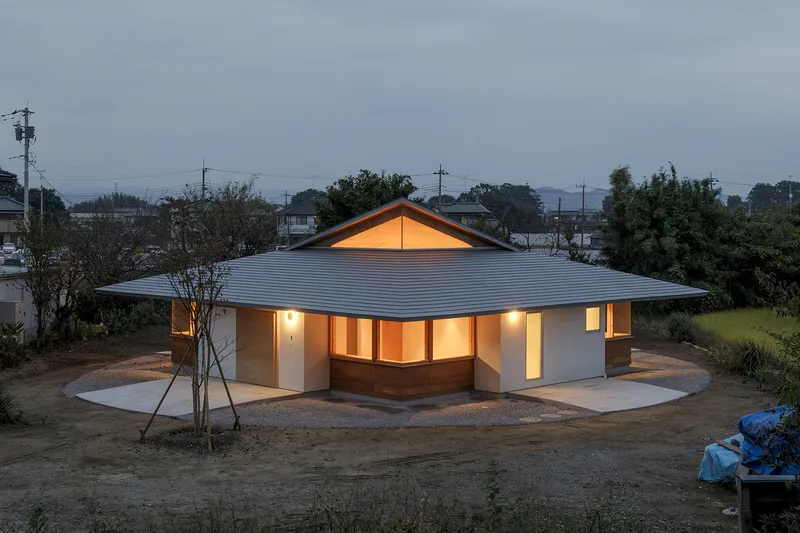 Corner view of the illuminated residence with pyramidal roof at dusk in a rural setting