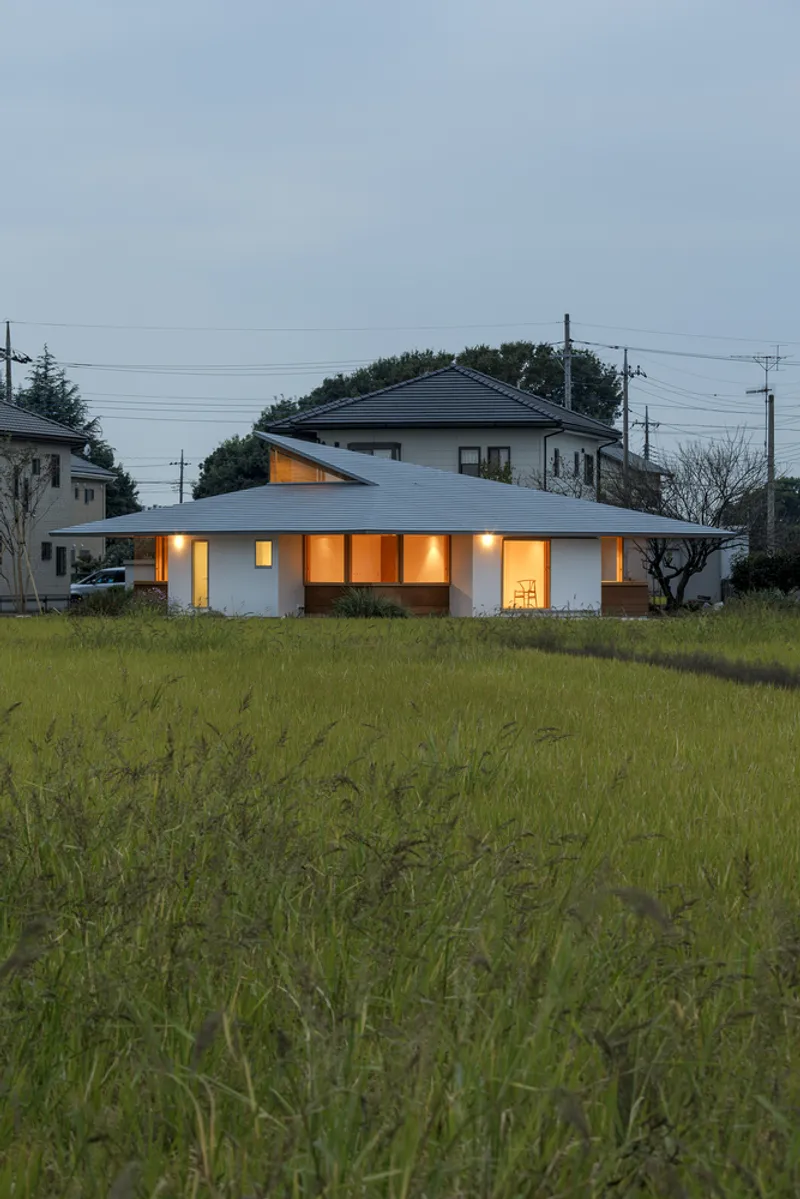 White single-story house with illuminated windows across a grassy field at dusk