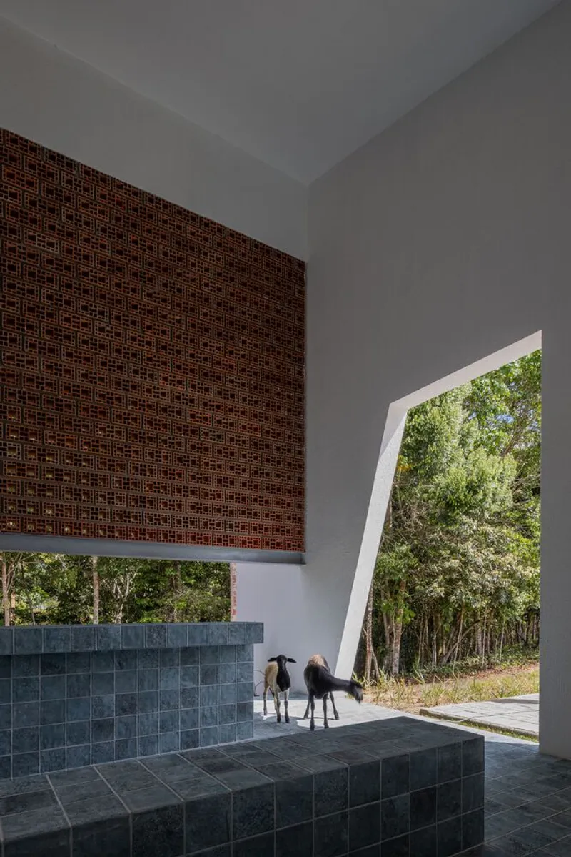 Covered terrace with woven brick screen above slate-tiled bench and angled opening framing trees