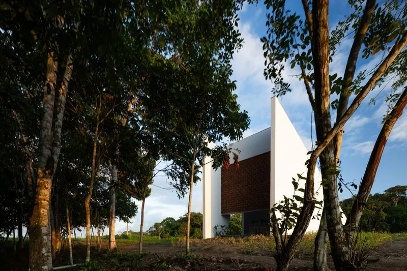 White sculptural volume with brick screen panel rising among eucalyptus trees at golden hour
