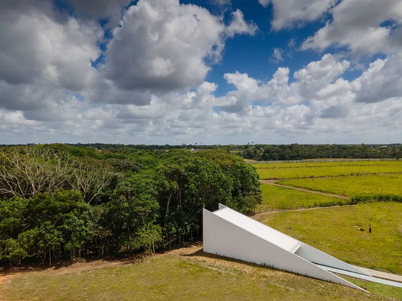 Distant view of the sloped white volume amid tree line and open grassland under cloudy sky